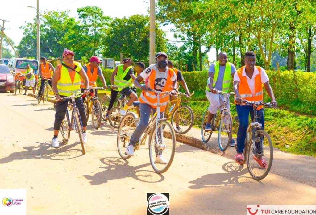 a group of people wearing reflective safety vests are riding on bikes down the side of a street with trees in the background