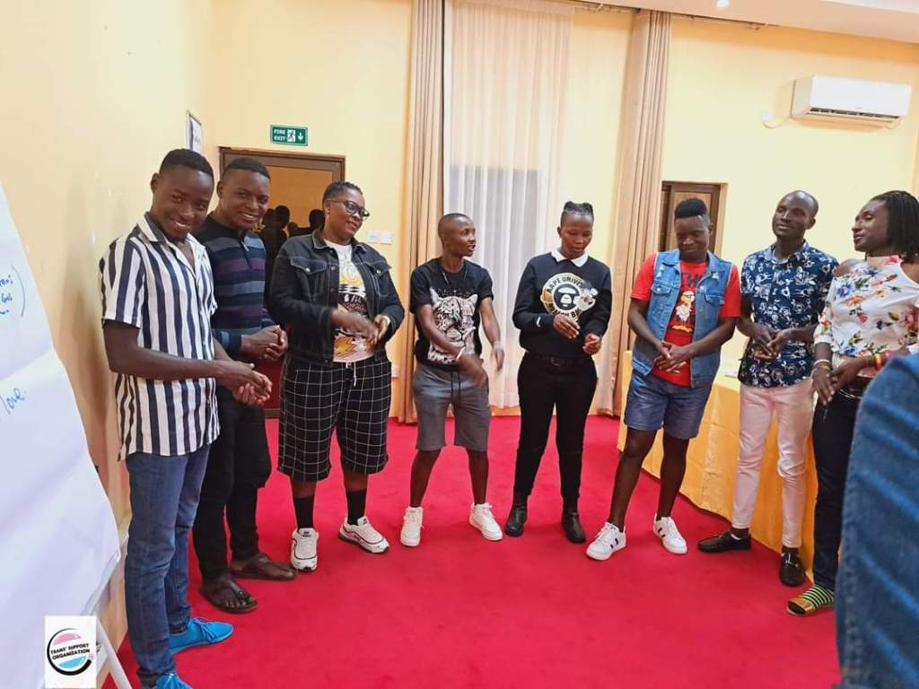 a group of 8 people gather while talking in a room with red carpet